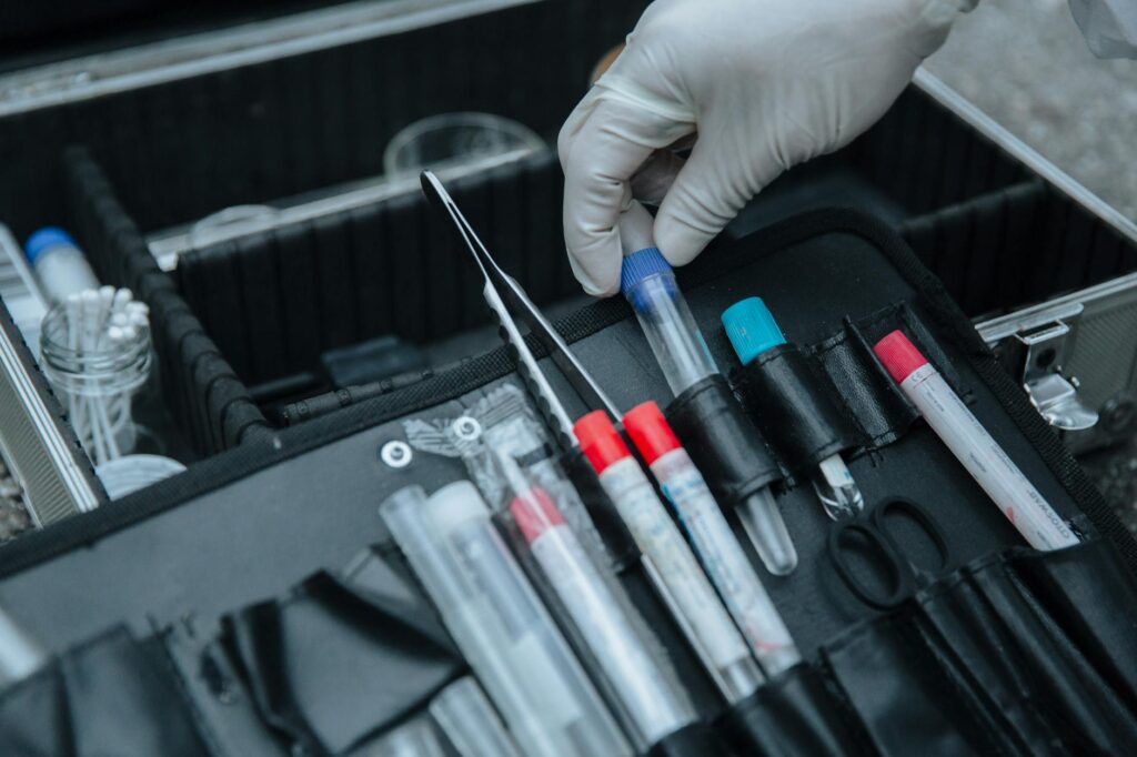 Gloved hand handling test tube in forensic equipment case at crime scene.